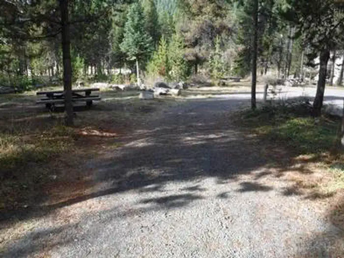 Gravel parking area next to picnic table and fire ring in pine forest with Lemolo Lake in the background