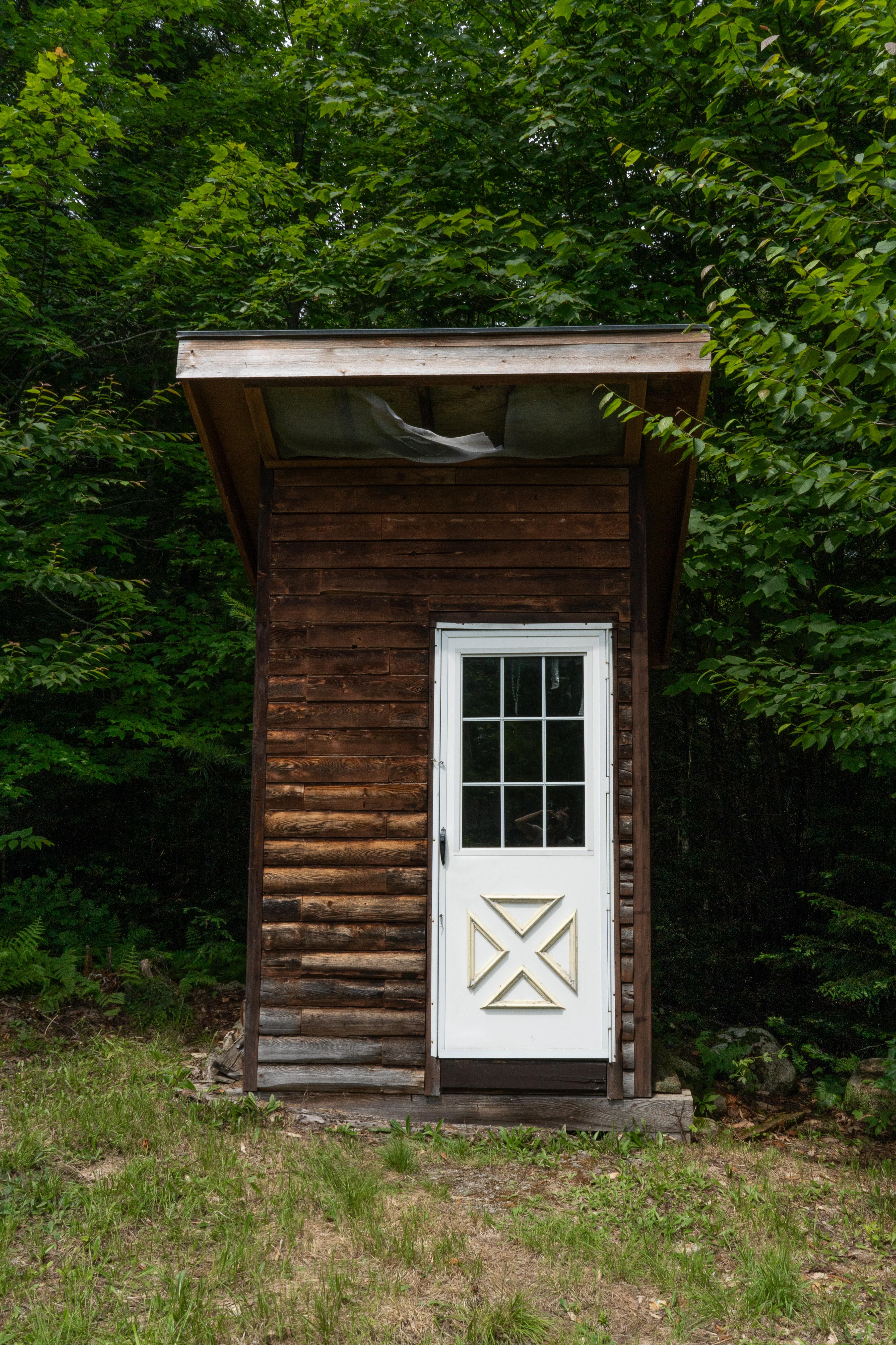 A wooden outhouse with a door in the woods
