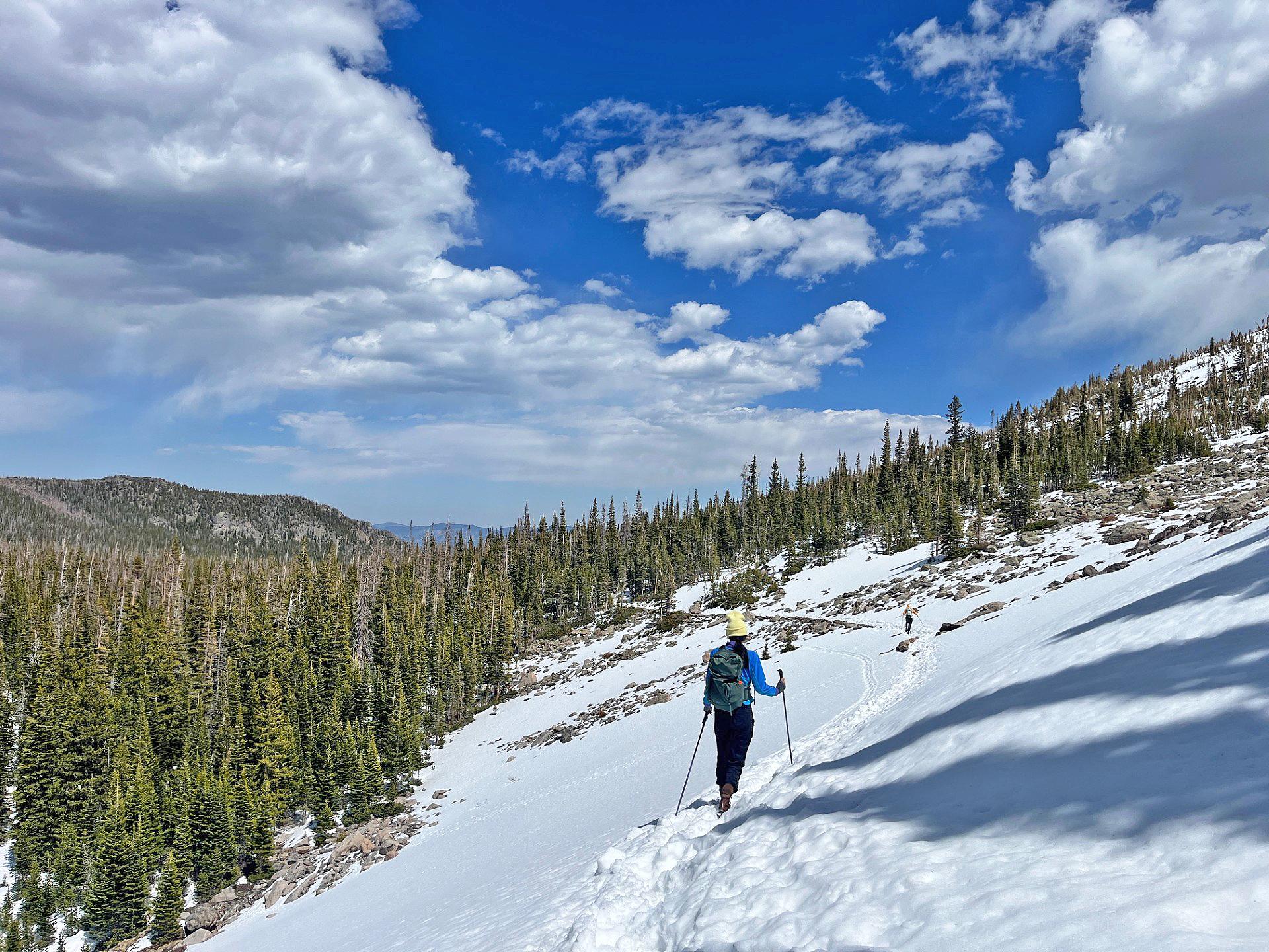 A person is using hiking poles and traction devices and hiking in snow