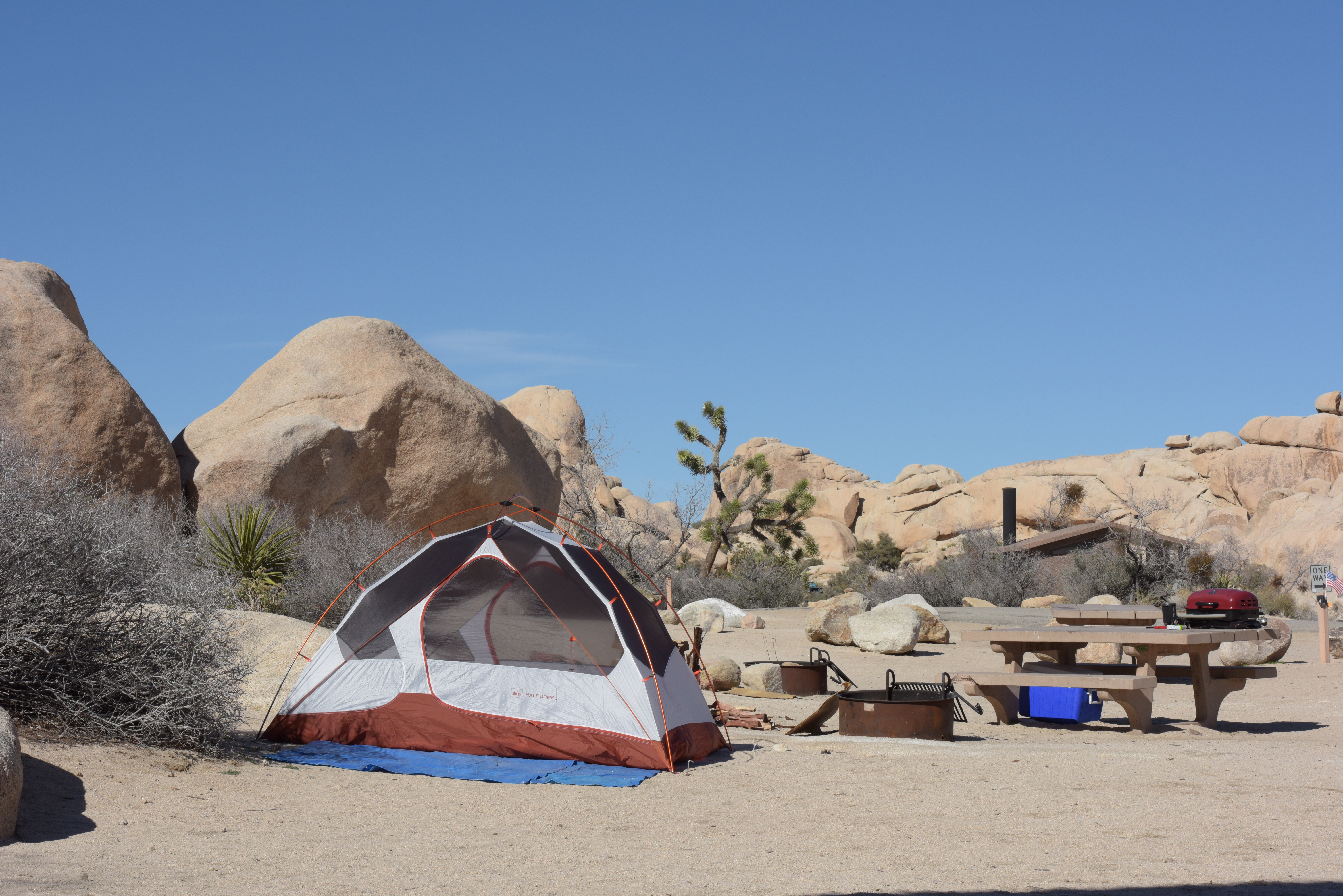 A tent, fire pit, picnic table are in a campsite surrounded by boulders.