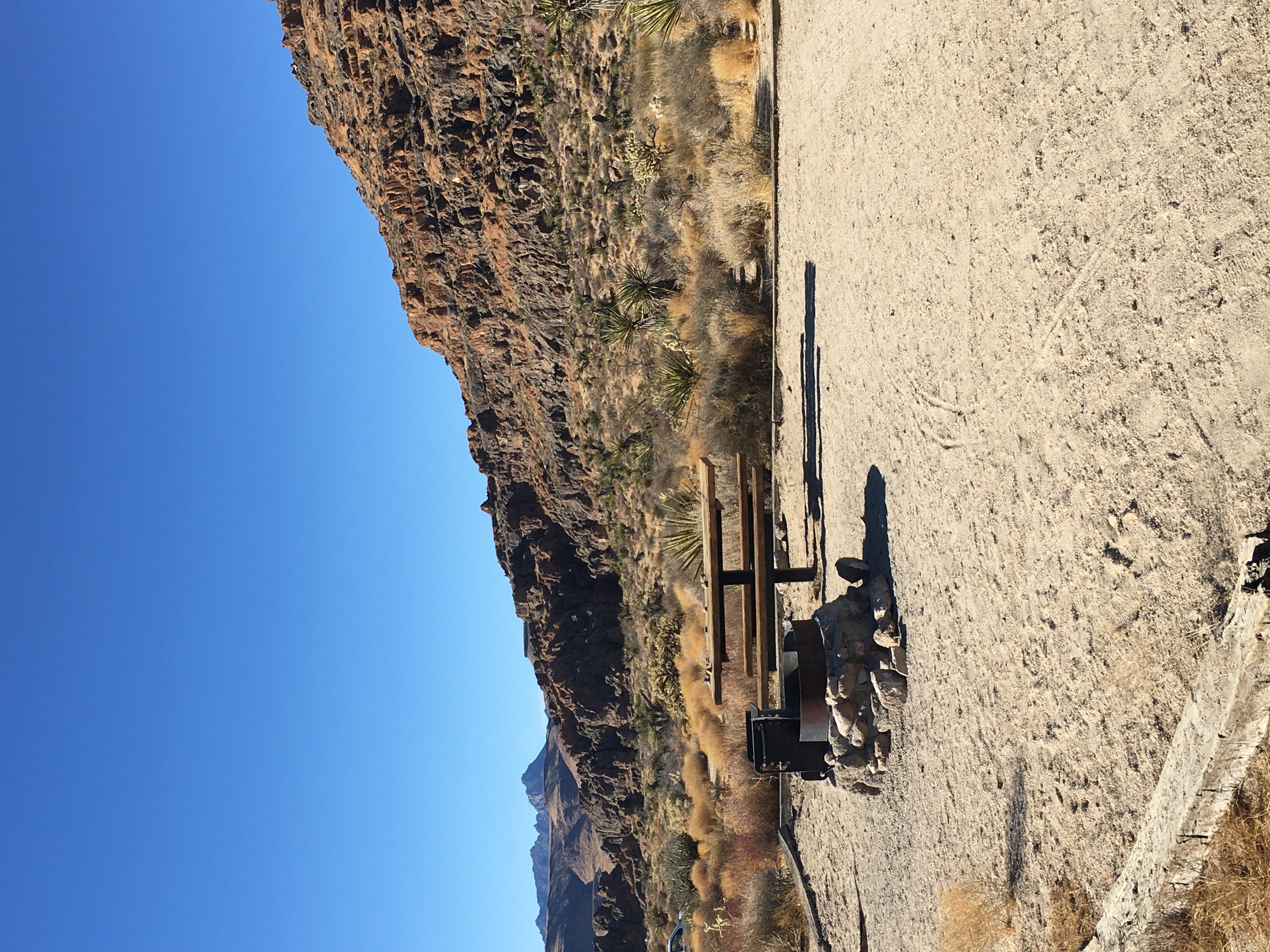 A rock fire ring and picnic table, with holey rock formations in the background